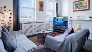 A modern living room with a sofa, a TV, and a small table. - Skyfall - 2 Bedroom Apartment - Milford Haven (Milford Haven)