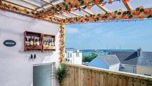 A balcony with a wooden pergola, a wine bottle shelf, and a view of the sea and buildings. - Skyfall - 2 Bedroom Apartment - Milford Haven (Milford Haven)