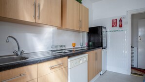 A modern kitchen with wooden cabinets, a stainless steel sink, and a black countertop. There are glass jars and colorful glasses on the counter. - Skyfall - 2 Bedroom Apartment - Milford Haven (Milford Haven)