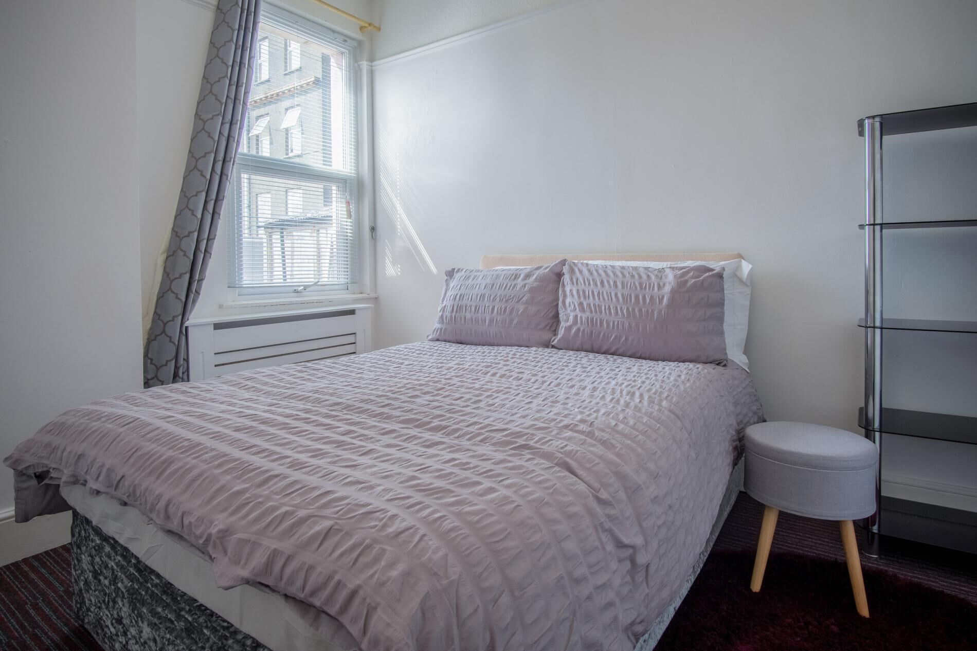 Una camera da letto con un letto, un comodino, una sedia, un termosifone e una finestra con tende.