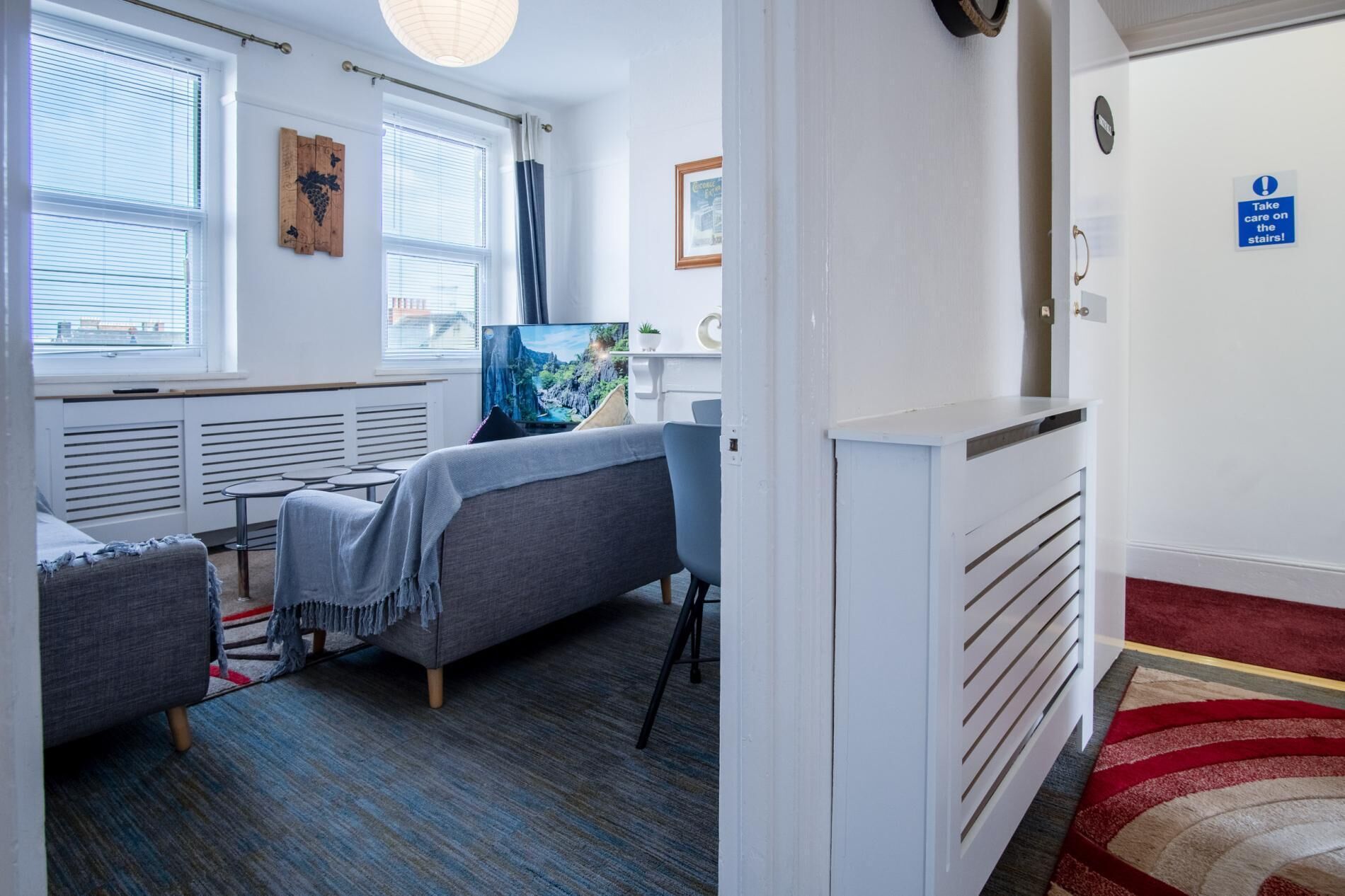 A room with a bed, a TV, a small table, and a window with blinds.