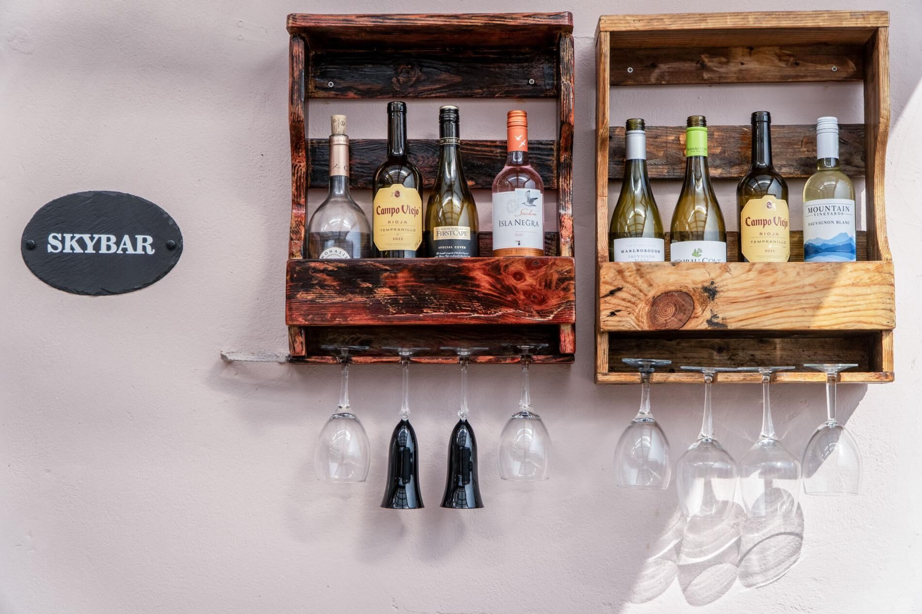 Two wooden wine racks with bottles and glasses against a wall, labeled 'SKYBAR'.