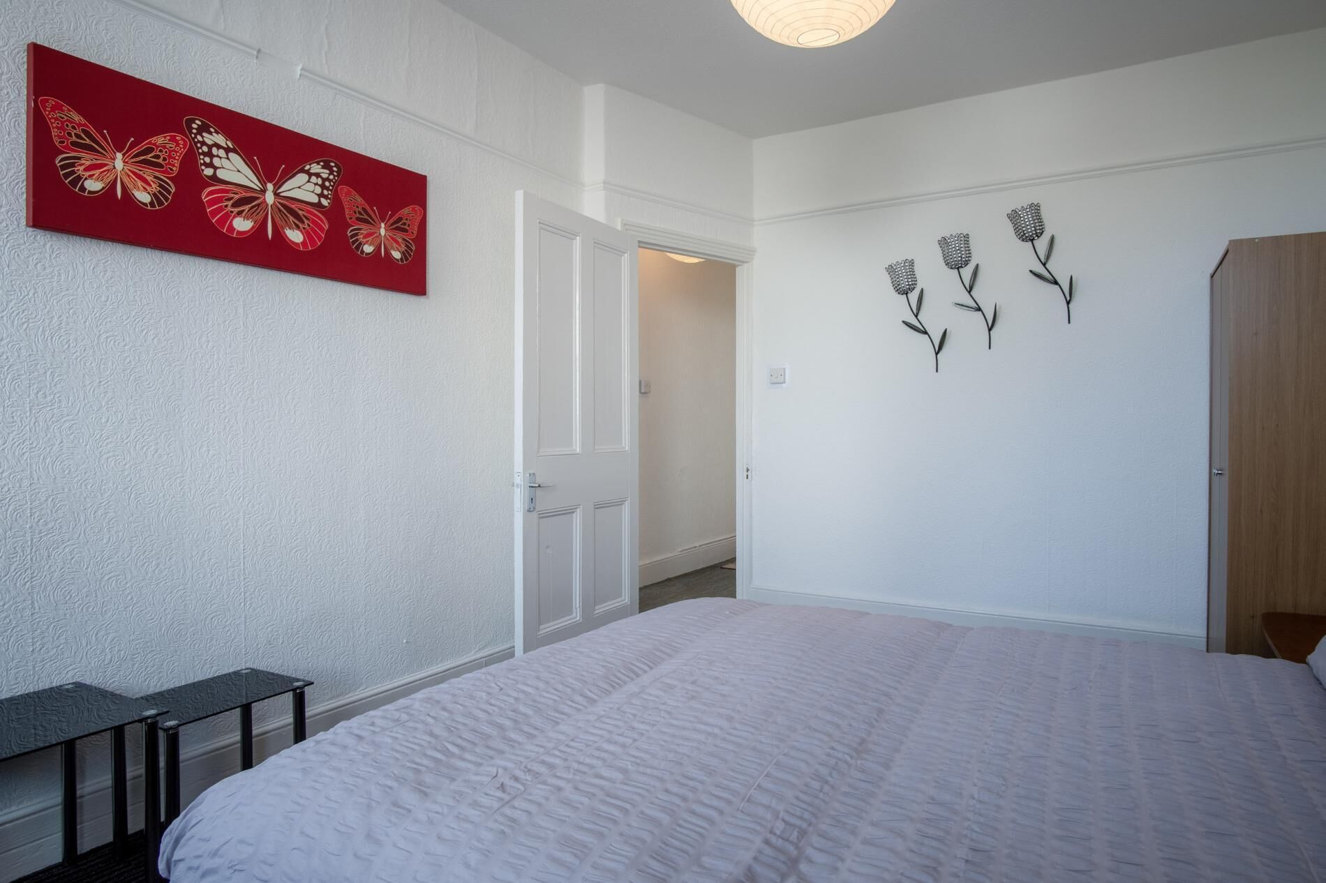 A bedroom with a bed, a door, a white textured wall, and a red artwork with butterflies.