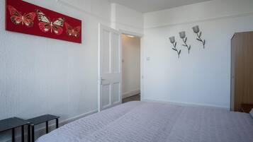 A bedroom with a bed, a door, a white textured wall, and a red artwork with butterflies.