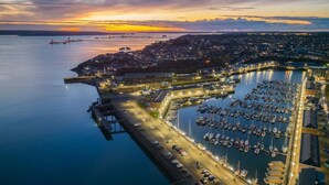 An aerial view of a marina with boats docked, a bridge, and a town in the background during sunset. - Skyfall - 2 Bedroom Apartment - Milford Haven (Milford Haven)