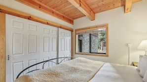 Une chambre avec un lit, une fenêtre donnant sur un mur en pierre et des poutres en bois au plafond.