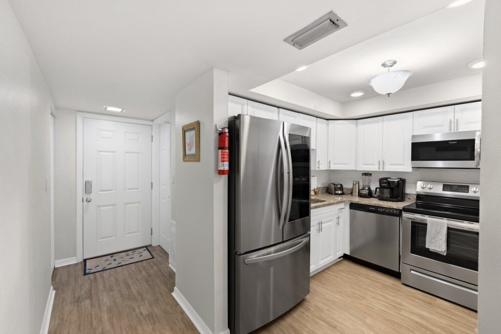 A modern kitchen with stainless steel appliances, white cabinetry, and a wooden floor.