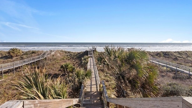 Une promenade en bois menant à la plage, bordée de palmiers, sous un ciel dégagé.