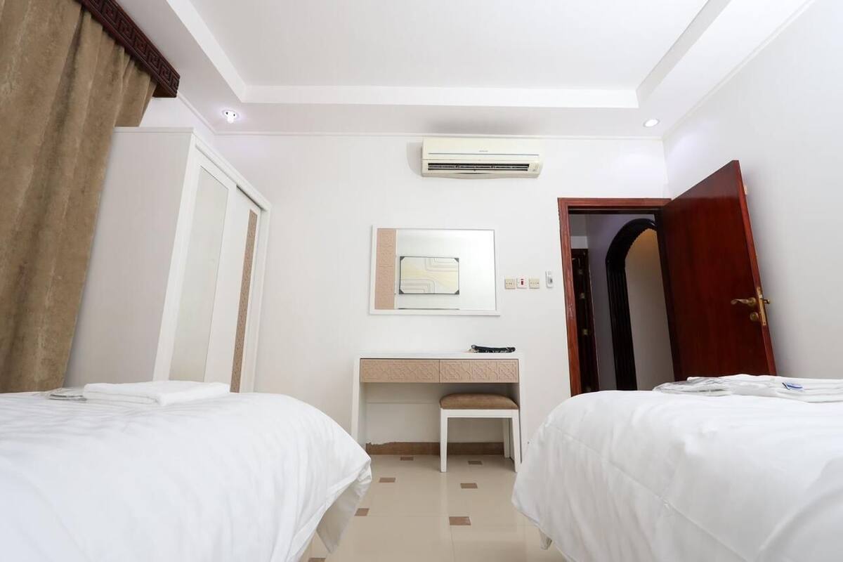 Habitación de hotel con dos camas, un escritorio, aire acondicionado y una puerta.