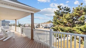 A wooden deck with white railings, a covered area, and a view of houses and pine trees. - 4-Bedroom 3 Bath Pet Friendly House w/Hot Tub, Pool, & Fence (Kitty Hawk)