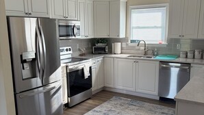 A modern kitchen with white cabinets, stainless steel appliances, a built-in oven, microwave, and dishwasher. - 4-Bedroom 3 Bath Pet Friendly House w/Hot Tub, Pool, & Fence (Kitty Hawk)