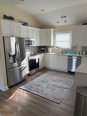 A modern kitchen with white cabinets, stainless steel appliances, a built-in oven, microwave, and dishwasher. - 4-Bedroom 3 Bath Pet Friendly House w/Hot Tub, Pool, & Fence (Kitty Hawk)