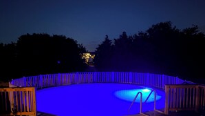 A swimming pool with a wooden deck and a blue-lit fence. - 4-Bedroom 3 Bath Pet Friendly House w/Hot Tub, Pool, & Fence (Kitty Hawk)