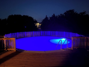 A swimming pool with a wooden deck and a blue-lit fence. - 4-Bedroom 3 Bath Pet Friendly House w/Hot Tub, Pool, & Fence (Kitty Hawk)