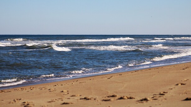 A beach with waves and footprints in the sand. - 4-Bedroom 3 Bath Pet Friendly House w/Hot Tub, Pool, & Fence (Kitty Hawk)