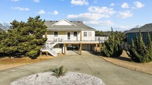 A two-story house with a covered porch and a staircase leading to the entrance. - 4-Bedroom 3 Bath Pet Friendly House w/Hot Tub, Pool, & Fence (Kitty Hawk)