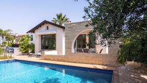 Une piscine bordée d’un muret en pierre et un espace patio aménagé avec des chaises longues.