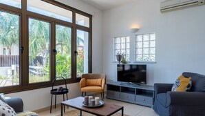Un salon moderne avec un canapé, une table basse, un téléviseur et de grandes fenêtres donnant sur un jardin.
