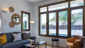 Un salon comprenant un canapé, un fauteuil, une table basse et de grandes fenêtres donnant sur une piscine et une clôture.
