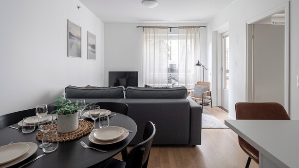 A modern living room with a sofa, a dining table set for four, and a television. - Homelike 1BR Apt with Sauna & Balcony at Pyynikki (Tampere)