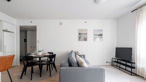 A modern living room with a grey sofa, a dining table with chairs, a TV on a stand, and a kitchen area visible through an open door. - Homelike 1BR Apt with Sauna & Balcony at Pyynikki (Tampere)