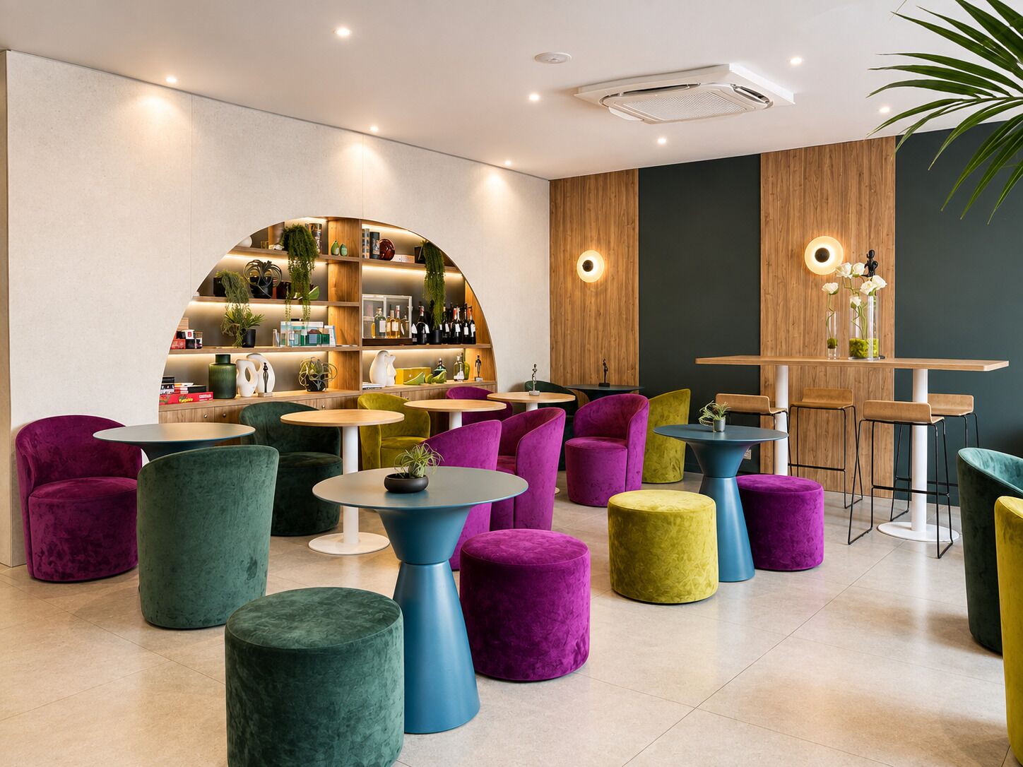 Un espace lounge moderne avec des tables rondes et des chaises colorées, un bar doté d’un comptoir en bois et une étagère incurvée agrémentée de plantes et de bouteilles.