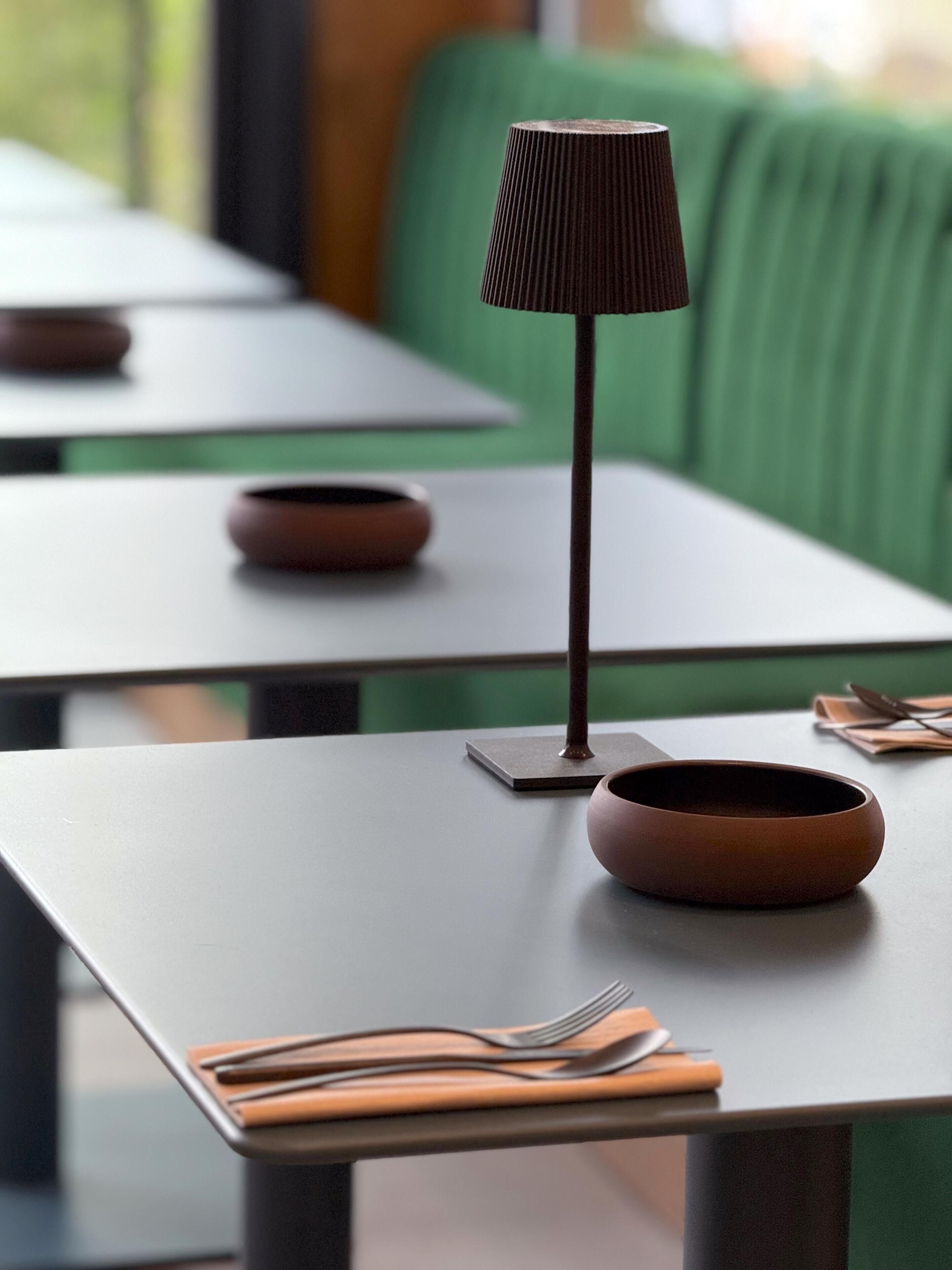 Una mesa de comedor con una lámpara oscura, un cuenco marrón y servilletas dobladas con cuidado.