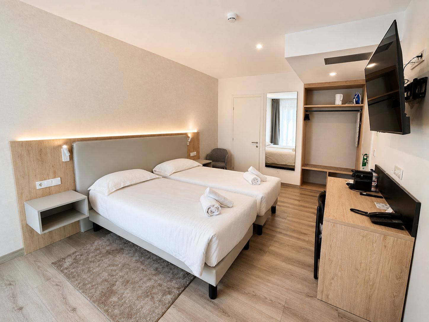 Een hotelkamer met twee bedden, een bureau, een televisie en een spiegel.