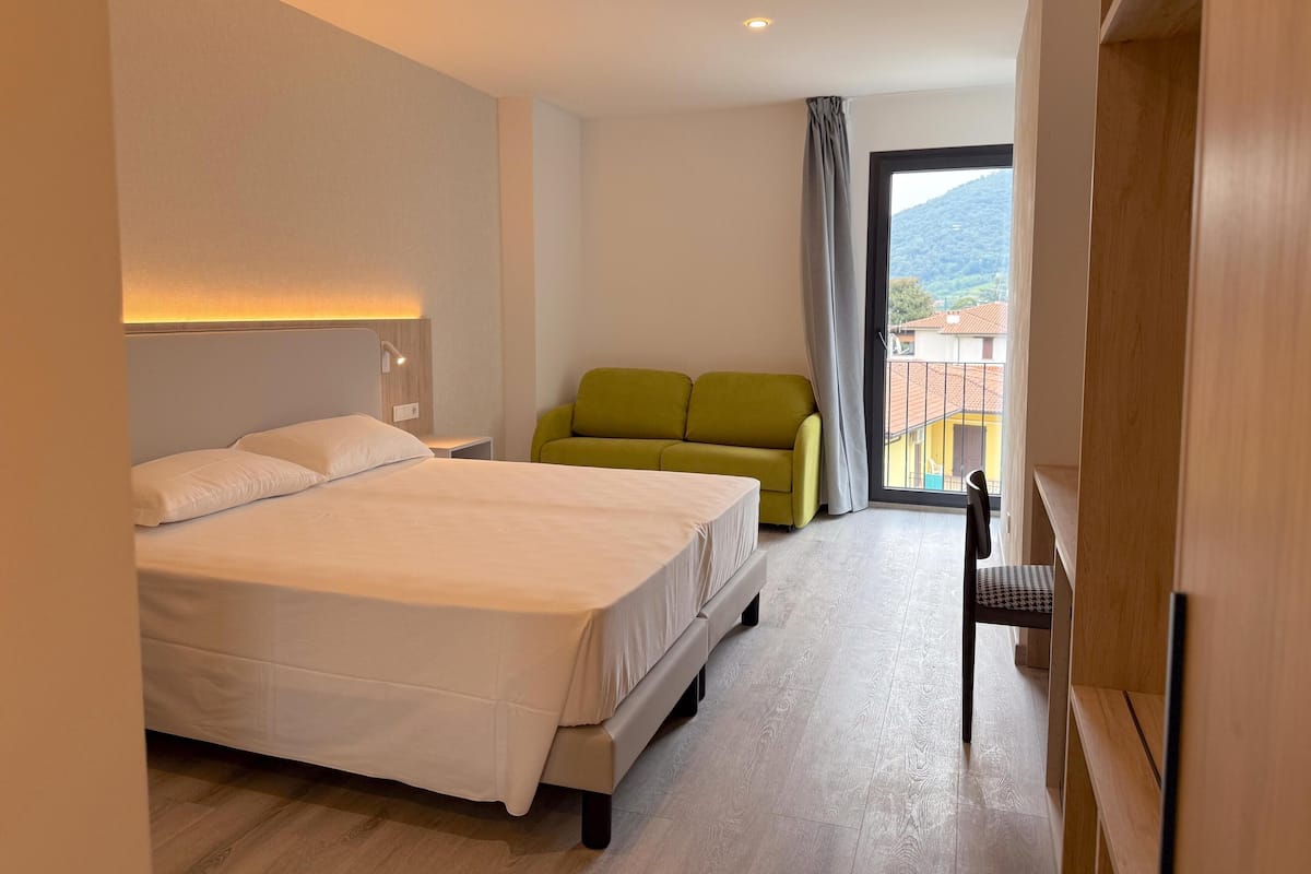 Une chambre d’hôtel avec un lit, un canapé vert, une petite table et une vue sur l’extérieur.