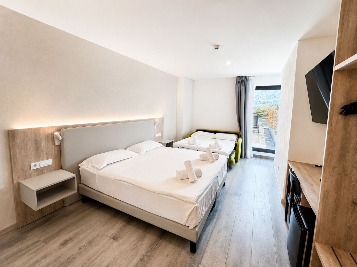 A hotel room with a large bed, bedside tables, a TV, and a view of the outdoors.