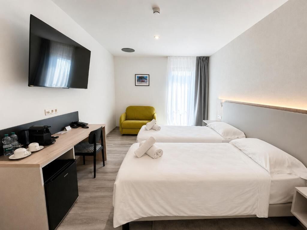 A hotel room with two beds, a desk, a chair, a television, and a window with curtains.