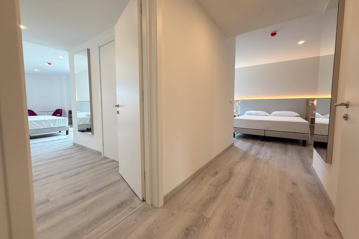 Une chambre d’hôtel moderne avec un plancher en bois, un lit avec une literie blanche, une table de chevet et une petite table de nuit.