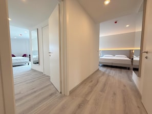 Una habitación de hotel moderna con suelo de madera, una cama con ropa de cama blanca, una mesita de noche y una lámpara de noche.