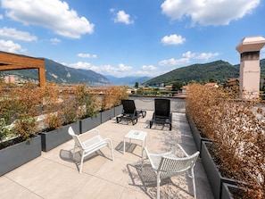 Una terraza con mobiliario exterior, vistas a montañas y un cuerpo de agua al fondo.