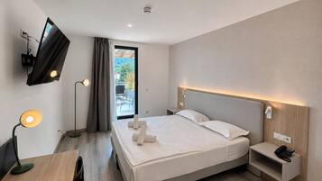 A modern hotel room with a bed, bedside table with a phone, a desk with a lamp, and a TV mounted on the wall.