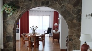 Un comedor con un arco de piedra, muebles de madera y vistas a una sala de estar con cortinas rojas y un ventanal.