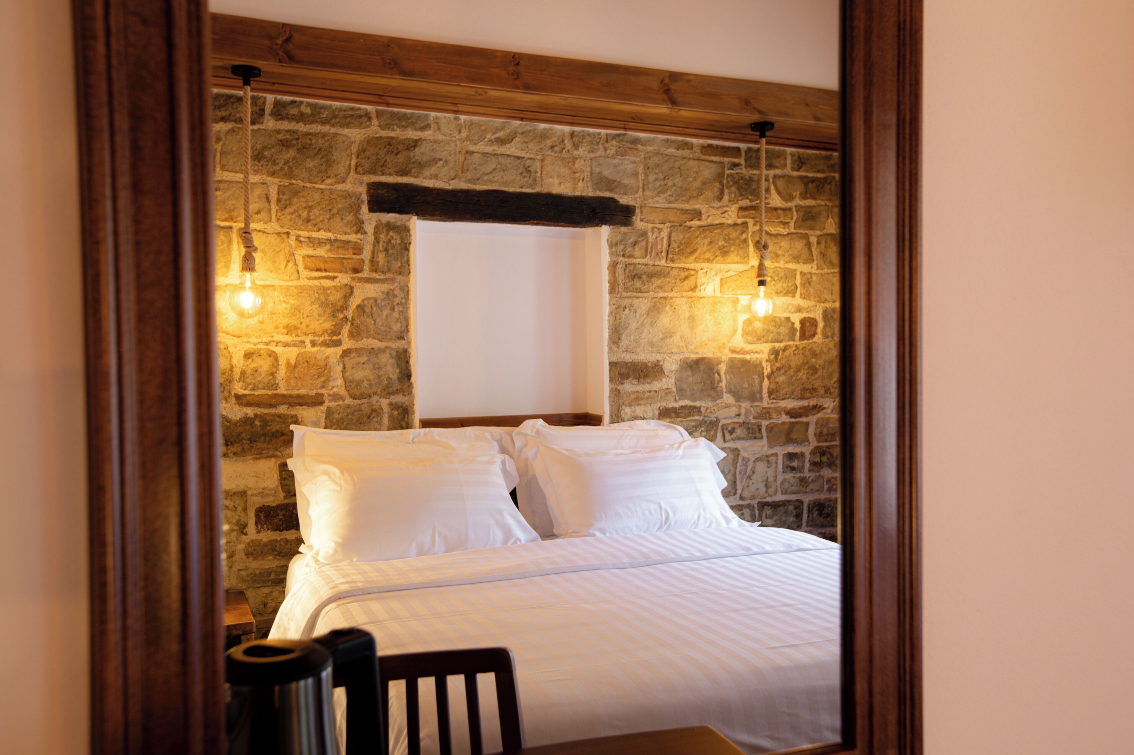 A room with a stone wall, a bed with white bedding, and two hanging light fixtures.