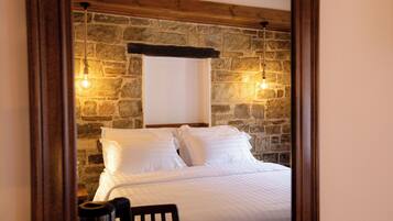 A room with a stone wall, a bed with white bedding, and two hanging light fixtures.