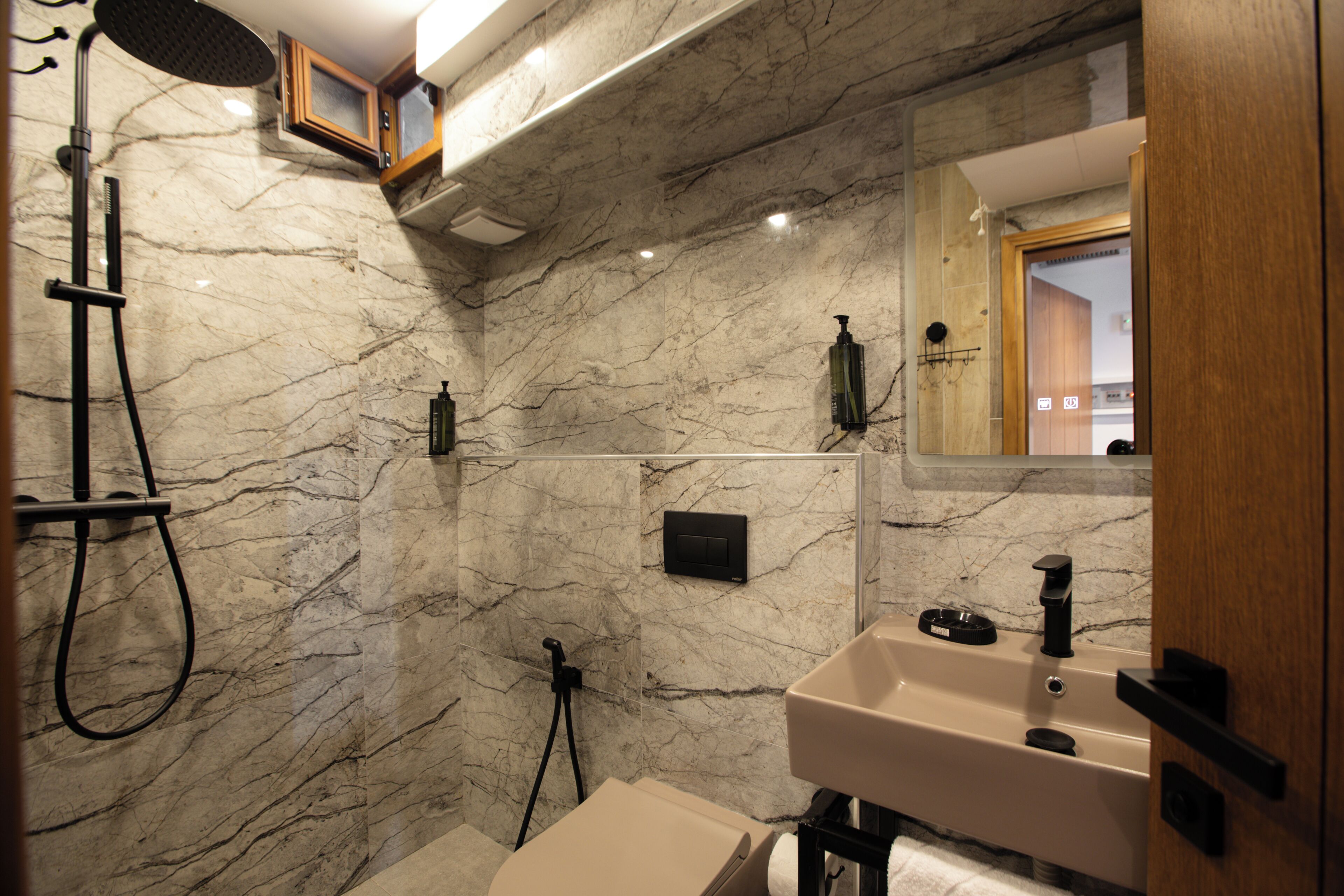 A bathroom with a marble wall, a shower, a sink, and a mirror.