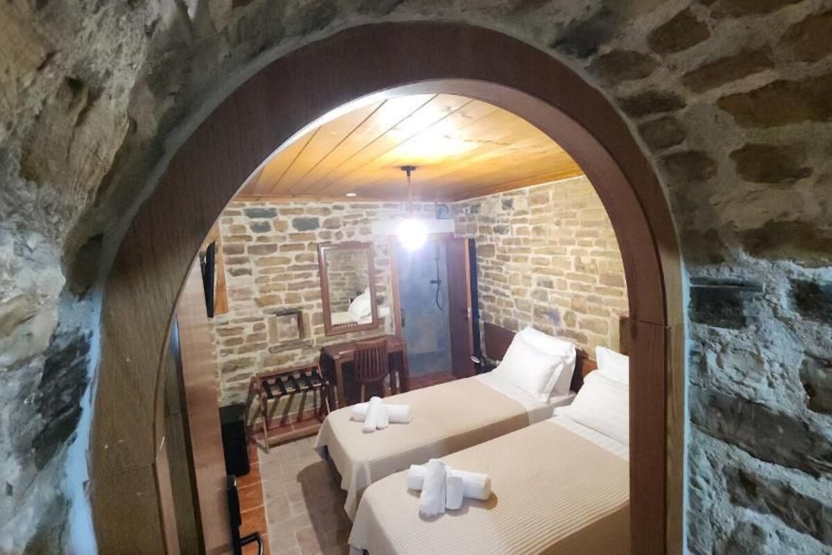 A stone-walled room with two beds, a desk, and a mirror.