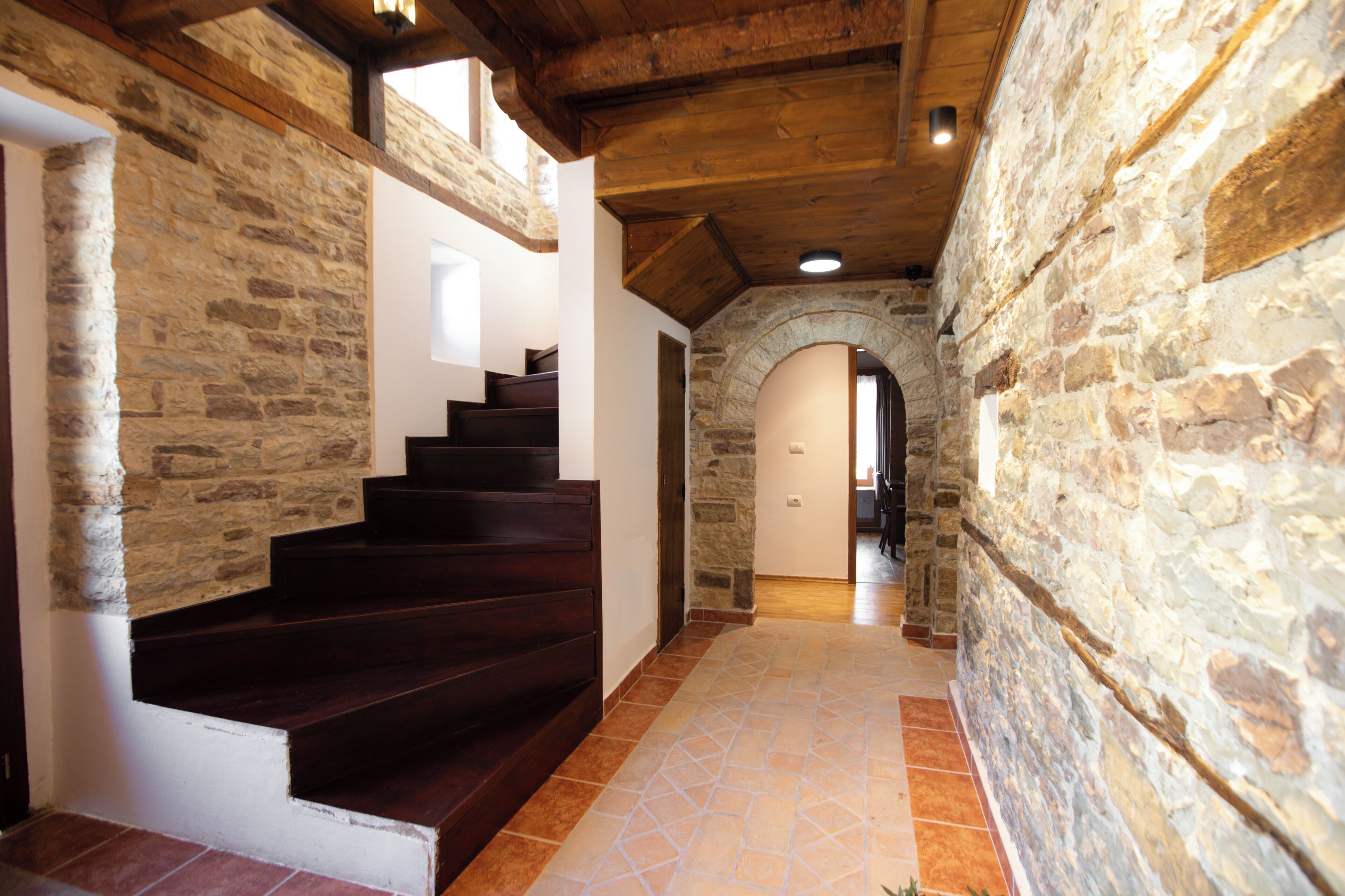 A staircase with stone walls and wooden beams, leading to an arched doorway.