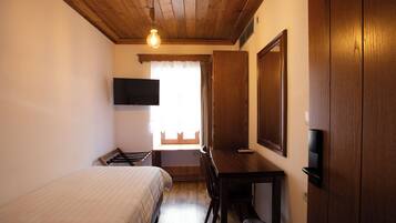 A room with a bed, a desk, a television mounted on the wall, and a window with curtains.