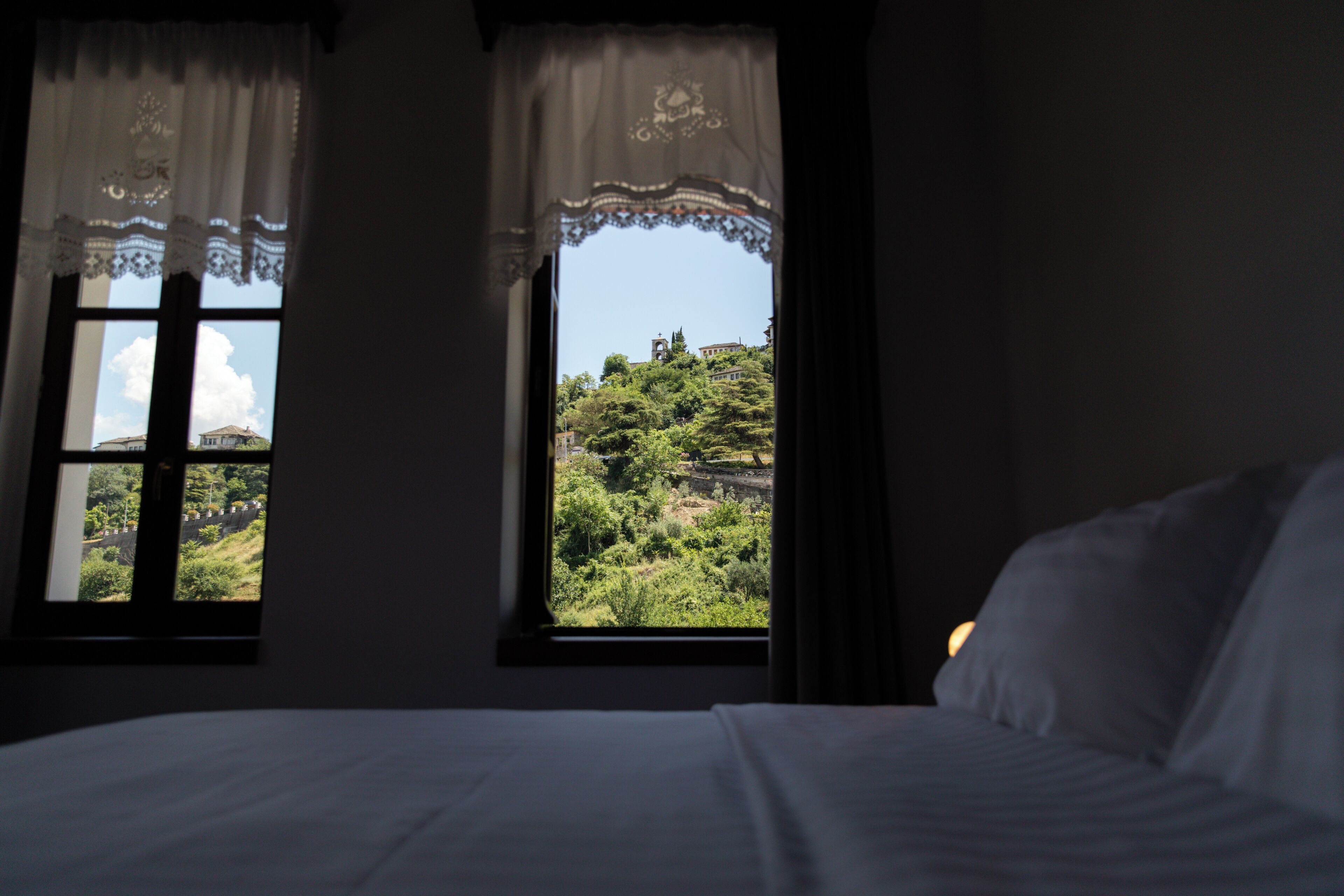 Ein Schlafzimmer mit zwei Fenstern, einem Bett und Blick auf eine grüne Landschaft.