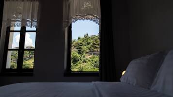 Ein Schlafzimmer mit zwei Fenstern, einem Bett und Blick auf eine grüne Landschaft.