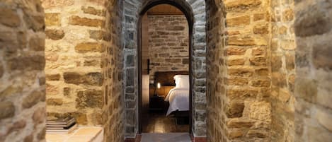 A stone corridor with an arched entrance leading to a room with a bed.