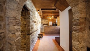 Un pasillo de paredes de piedra que conduce a un interior de madera con suelo de baldosas y una lámpara colgante.