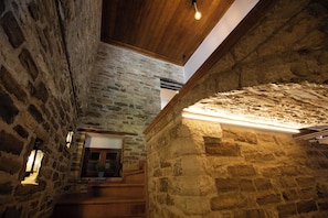 A stone interior with a wooden staircase, a window with a view, and a ceiling light fixture. - Bizant House Boutique Hotel (Gjirokastër)