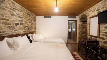 Habitación con dos camas, techo de madera, paredes de piedra, televisor y puerta que da a un baño.