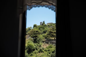 A view through a window with a decorative frame, featuring a building with a bell tower on a hill, surrounded by greenery. - Bizant House Boutique Hotel (Gjirokastër)