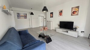Un soggiorno moderno con un divano blu, un tavolino in vetro, una TV a schermo piatto e un arredamento minimalista.